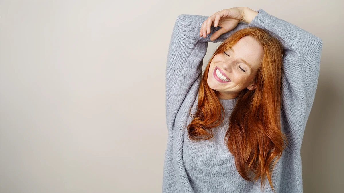 A content, smiling redheaded girl in a gray sweater with a big bright smile and white teeth